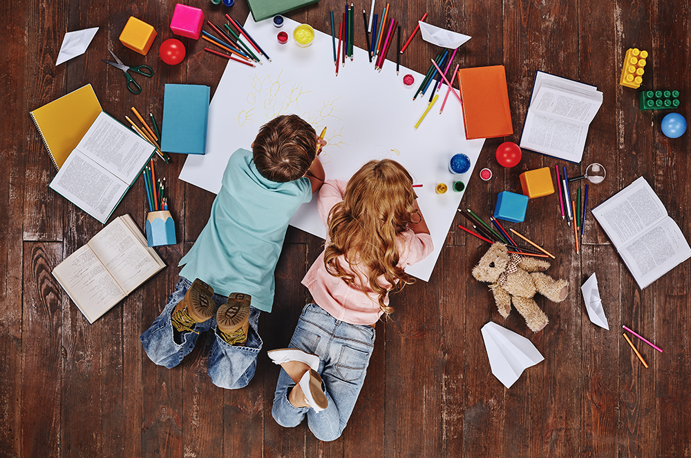 Play Is The Work Of Childhood. Children Lying Near Books And Toys, While Drawing